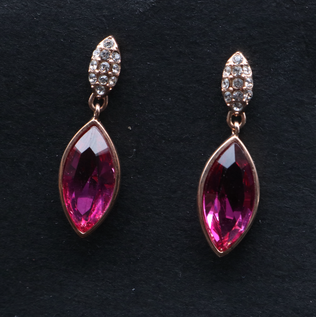 A pair of gold-plated stainless steel earrings with a central pink gemstone and smaller clear crystal embellishments.