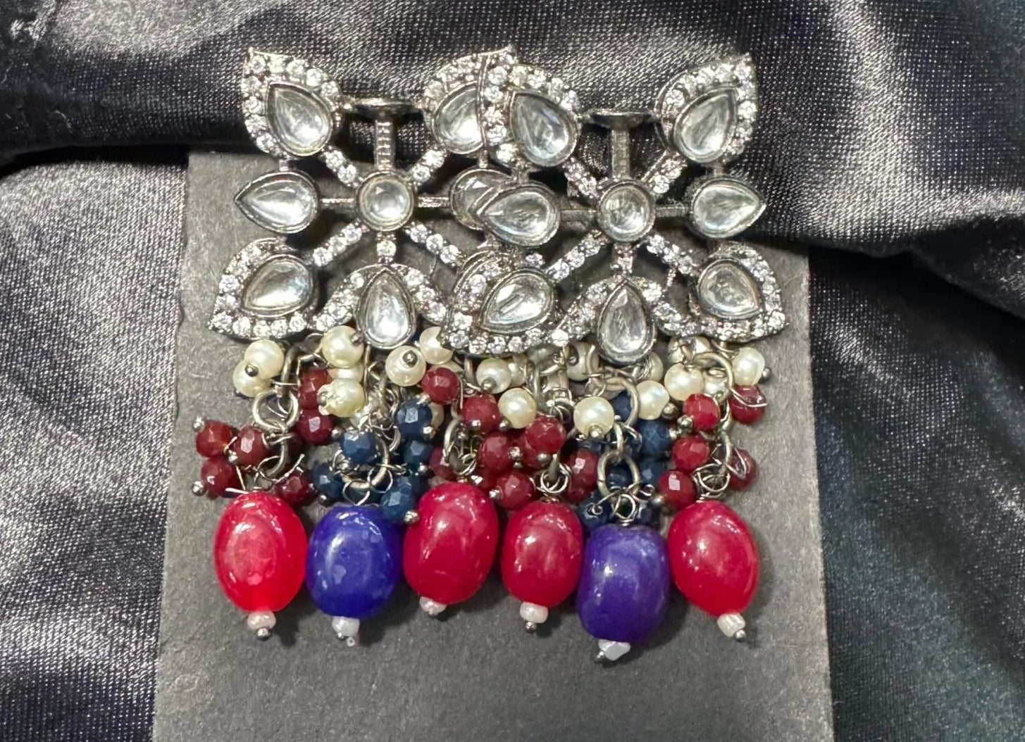 Earrings with a decorative brooch and colorful beads on a dark fabric background