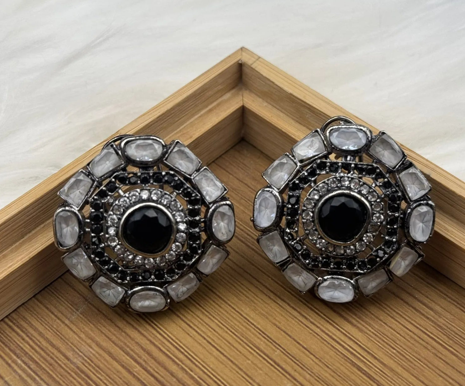 Pair of ornate gold-plated and American diamonds earrings with black centers on a wooden surface.