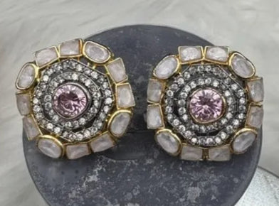 Pair of ornate gold-plated and American diamonds earrings with pink gemstones on a textured surface
