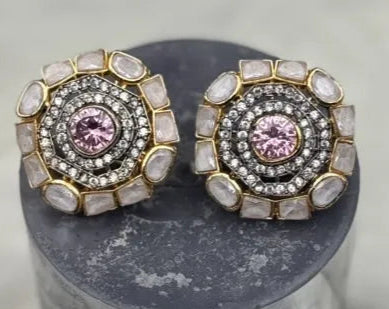 Pair of gold-plated and American diamonds earrings with pink gemstones and gold accents on a gray cylindrical stand.