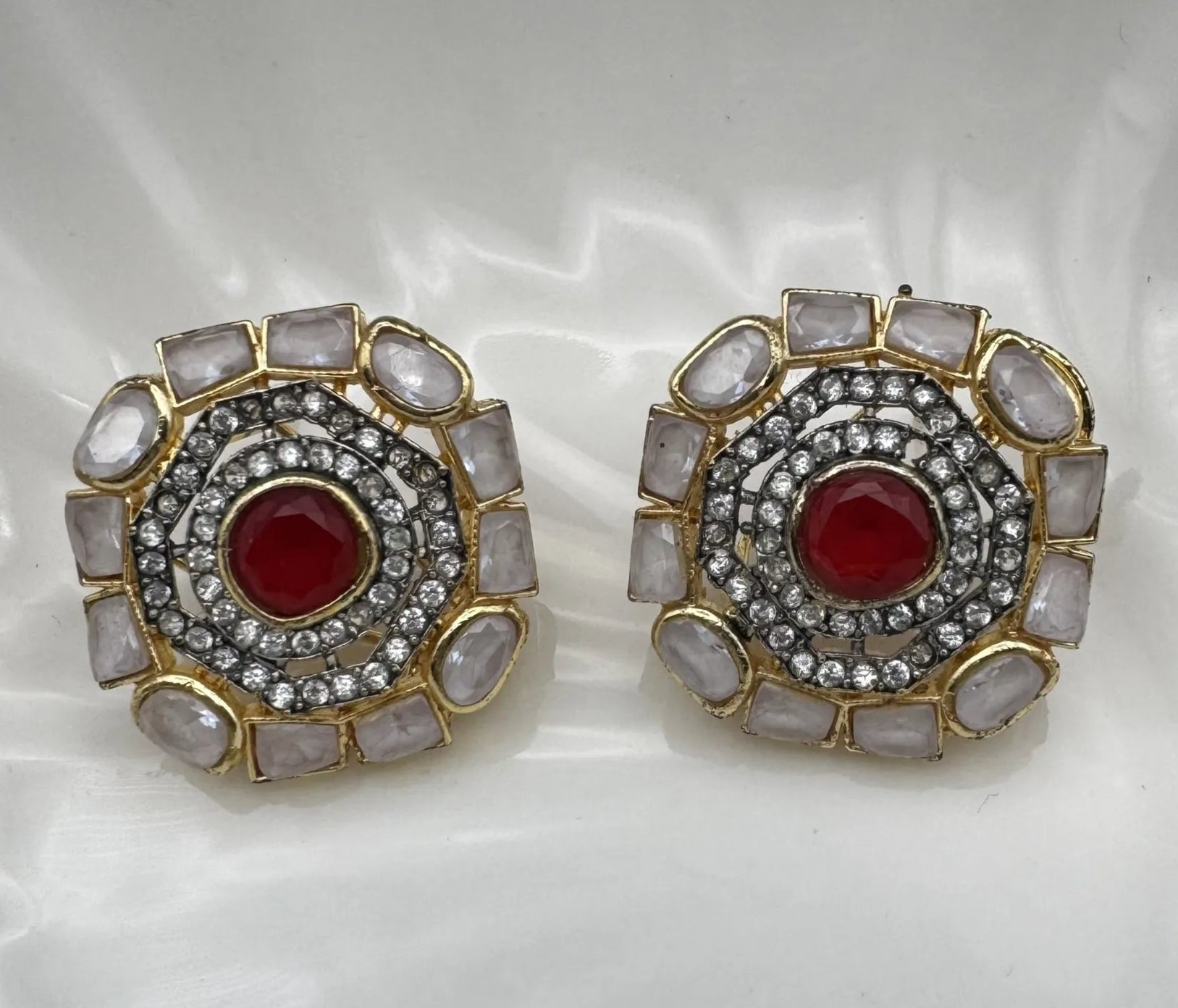 Pair of gold-plated and American diamonds earrings with red center and gold and silver accents on a white background