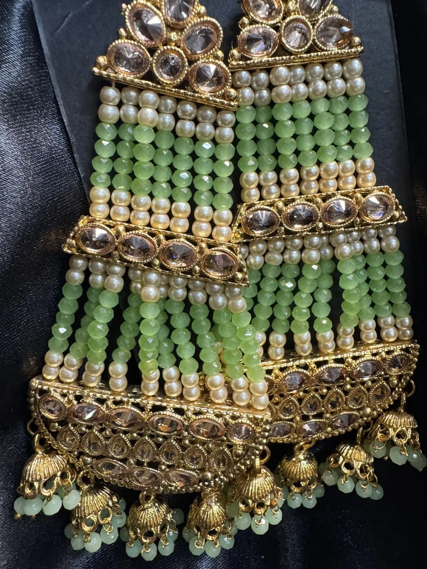 Ornate jewelry piece with green beads and gold accents on a black background