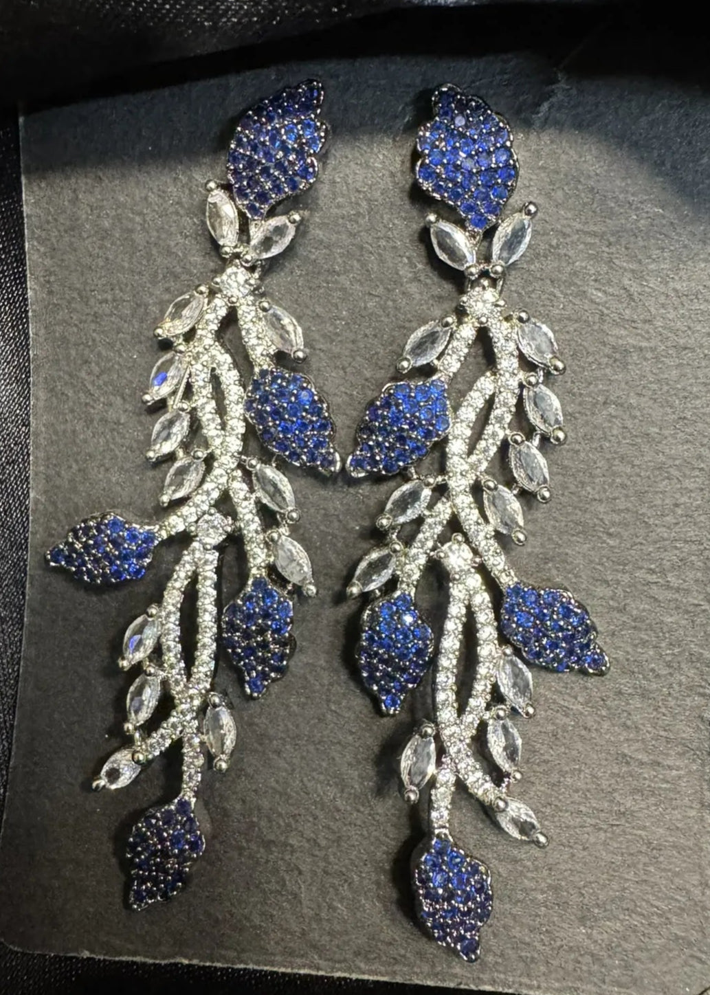 Pair of blue and silver earrings on a gray card against a black satin background