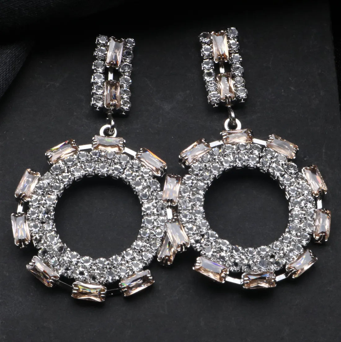 Pair of silver American diamonds earrings with circular designs and clear stones on a dark background