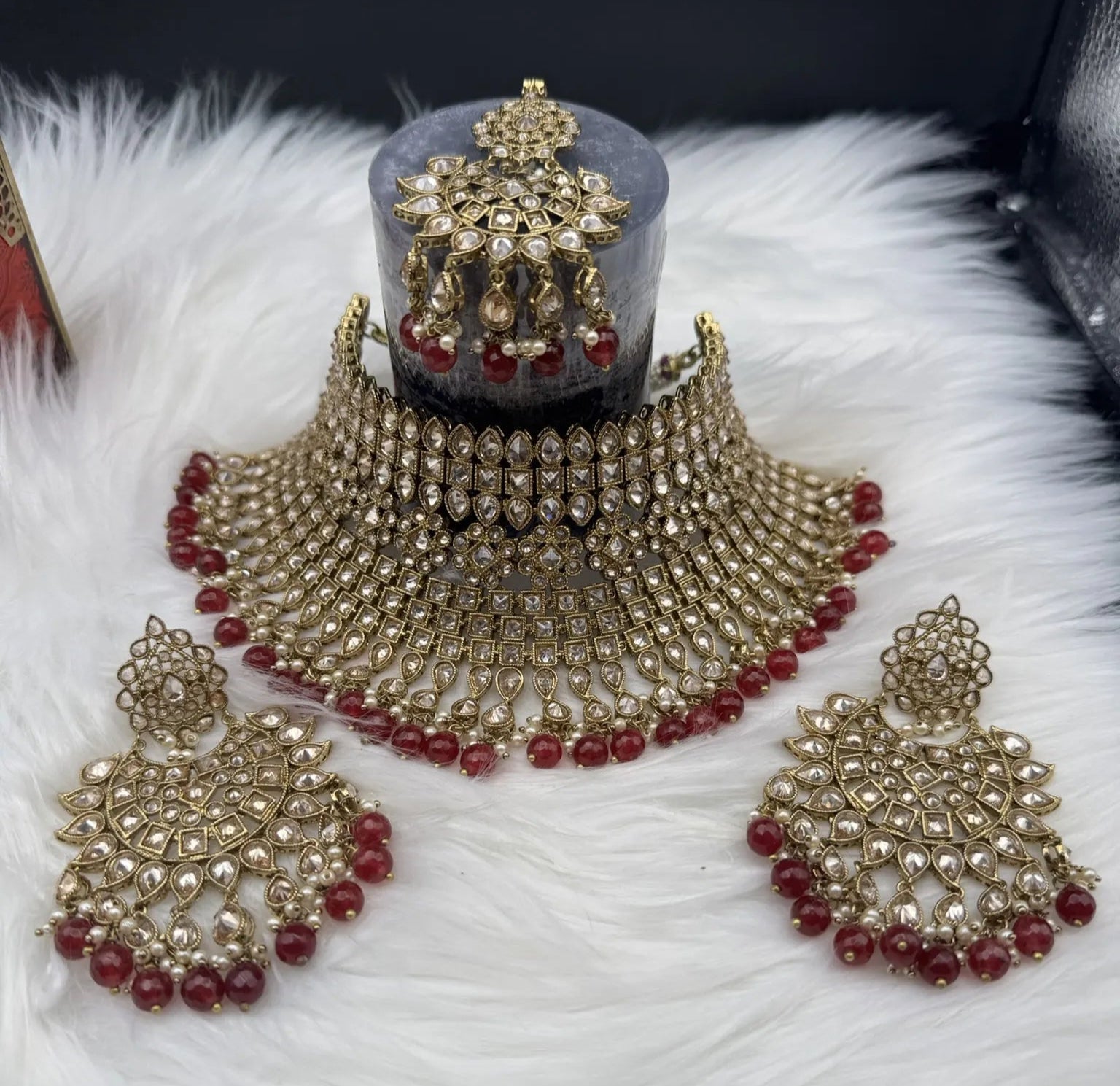 Ornate gold-plated, waterproof Indian bridal set with red hanging beads and matching teeka and earrings on a black background