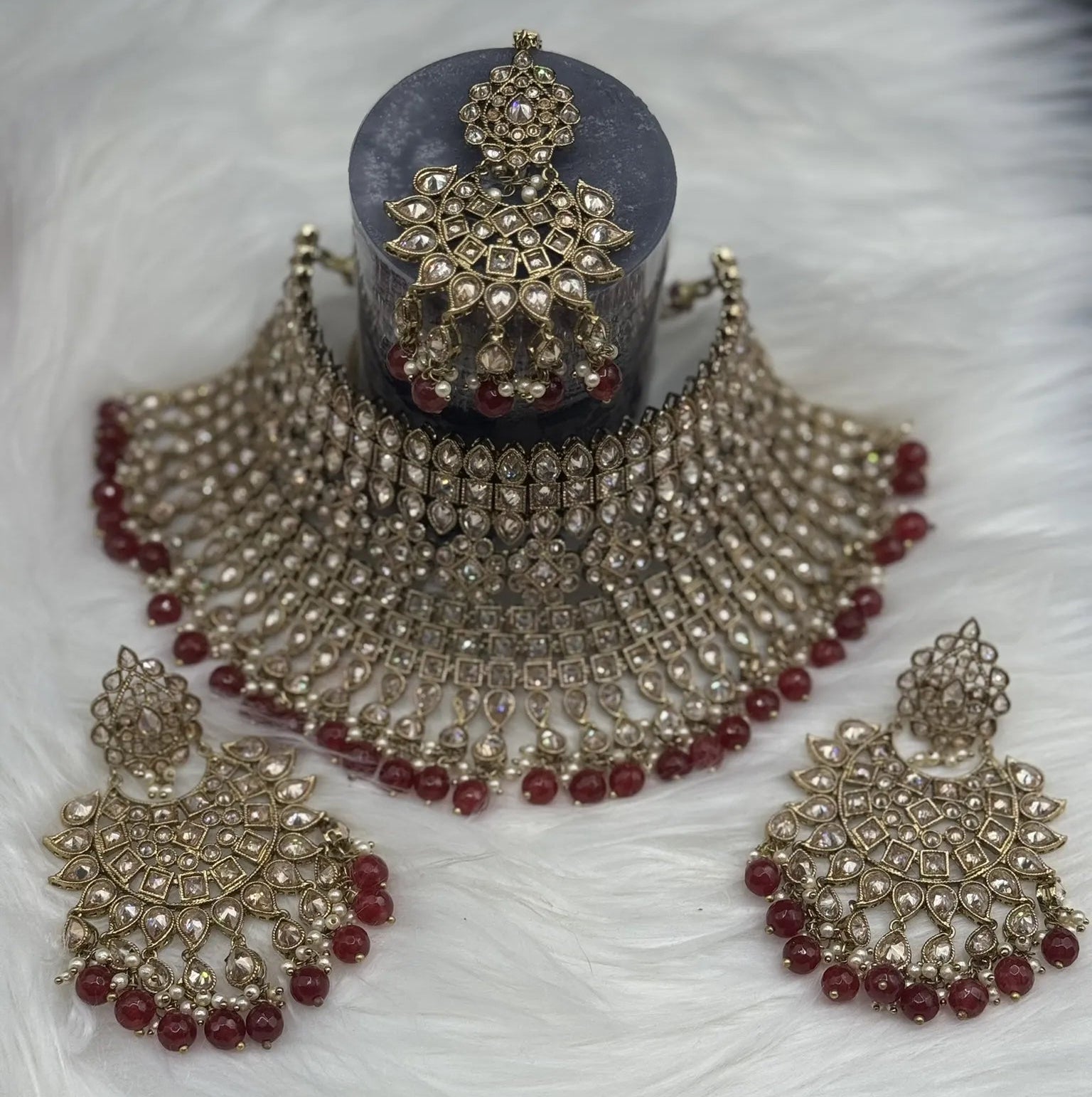 top view of gold-plated, waterproof Indian bridal set with red hanging beads and matching teeka and earrings on a black background