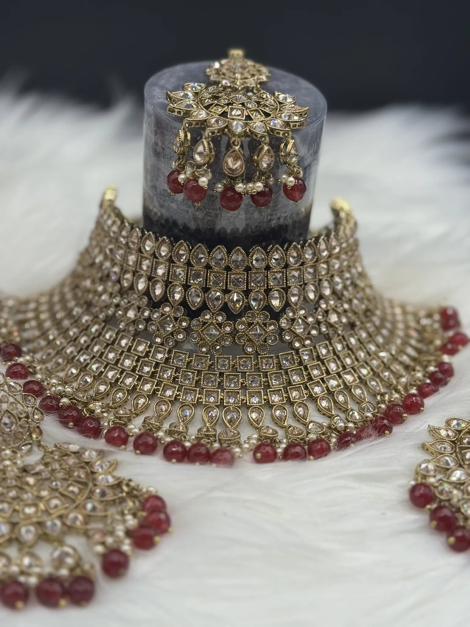 front view of gold-plated, waterproof Indian bridal set with red hanging beads and matching teeka and earrings on a black background