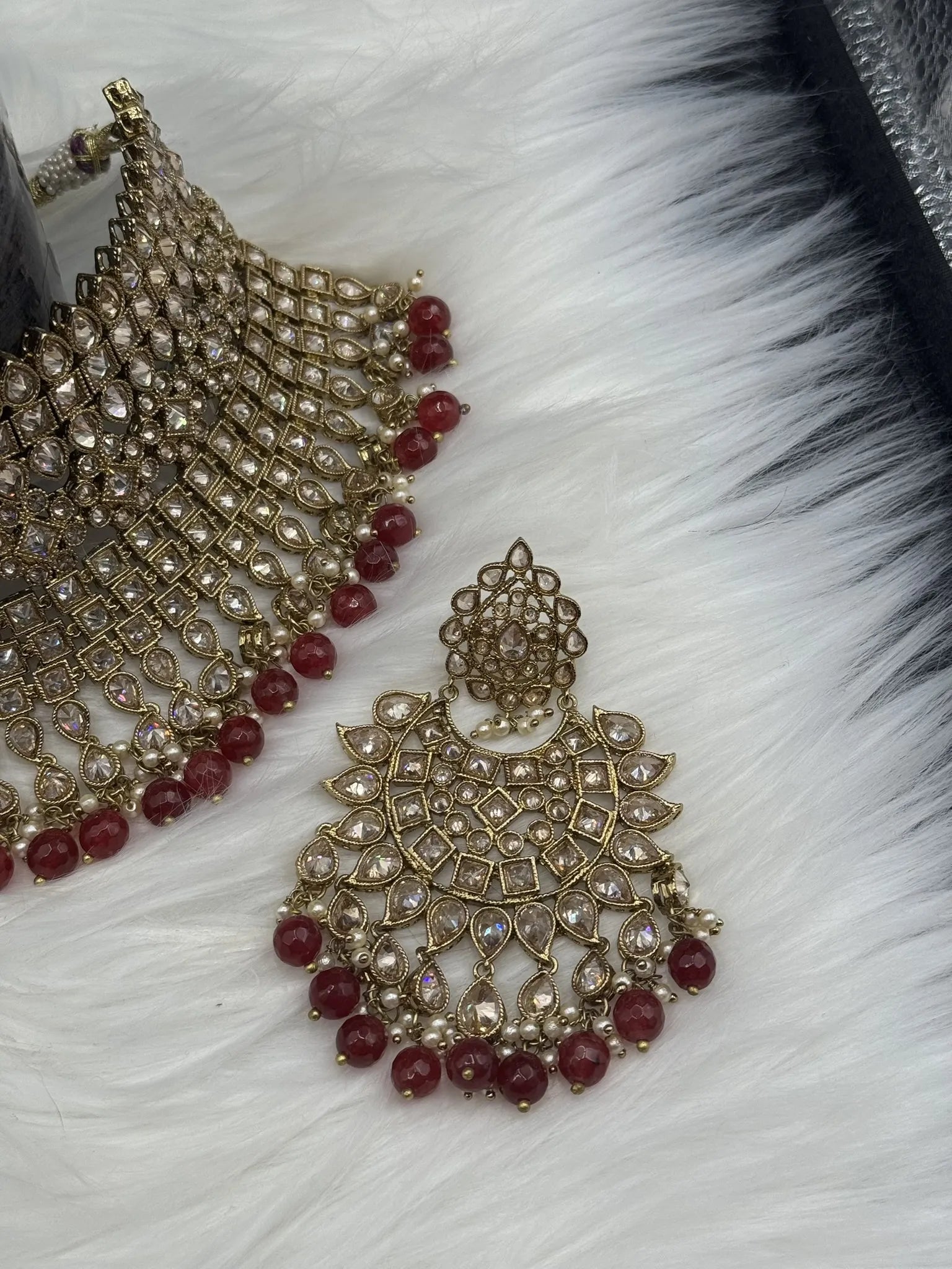 earring view of gold-plated, waterproof Indian bridal set with red hanging beads and matching teeka and earrings on a black background