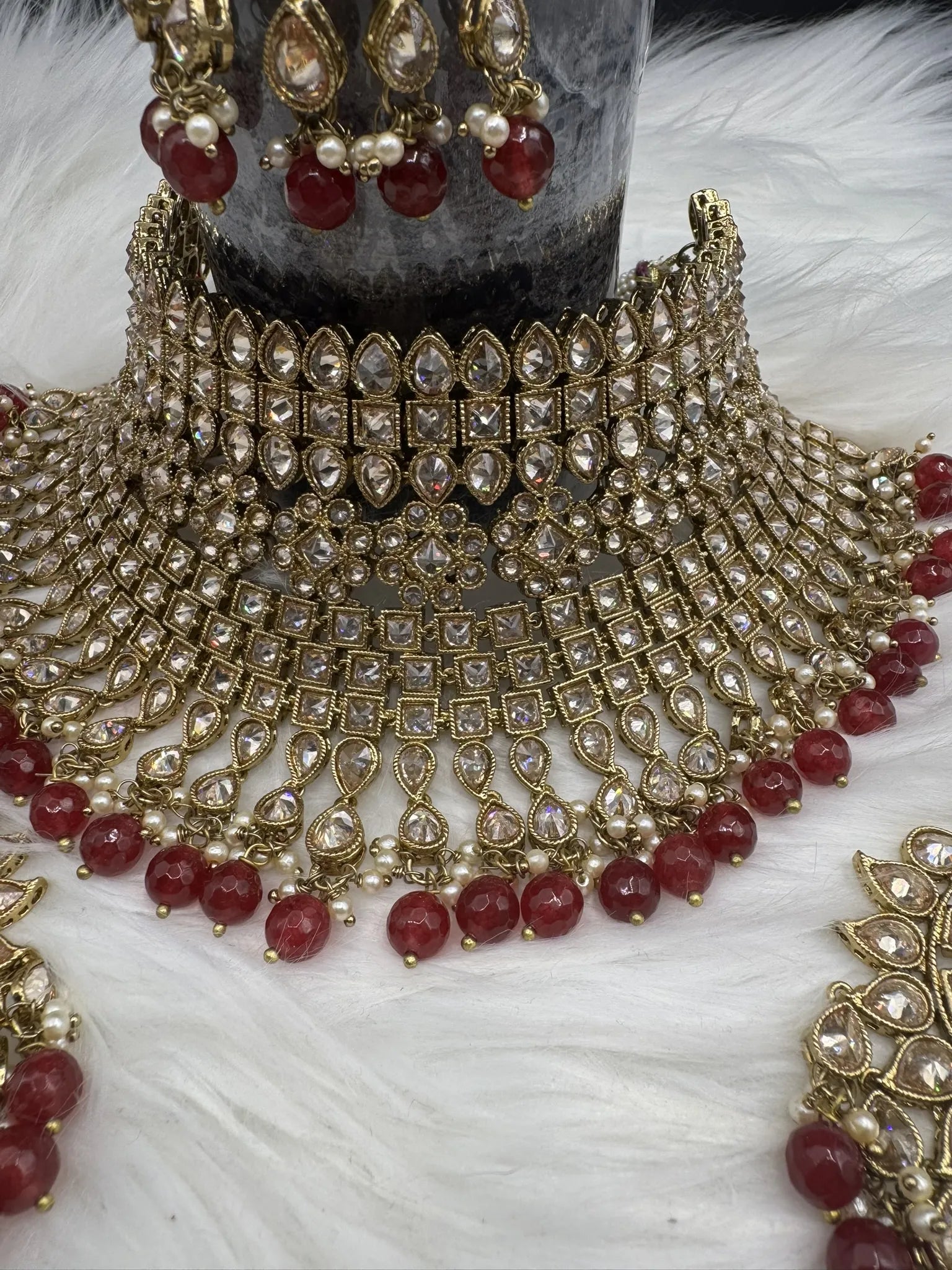 front view of gold-plated, waterproof Indian bridal set with red hanging beads and matching teeka and earrings on a black background