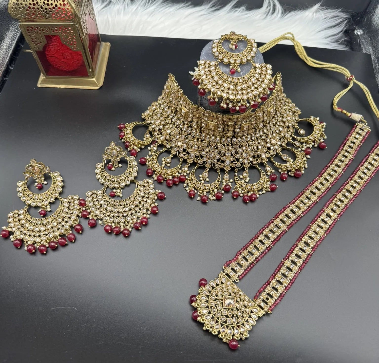 top view of complete exquisite gold-plated Indian bridal set with red accents, sparkling stones & matching earrings, teeka and a long traditional necklace. Waterproof & anti-tarnish.