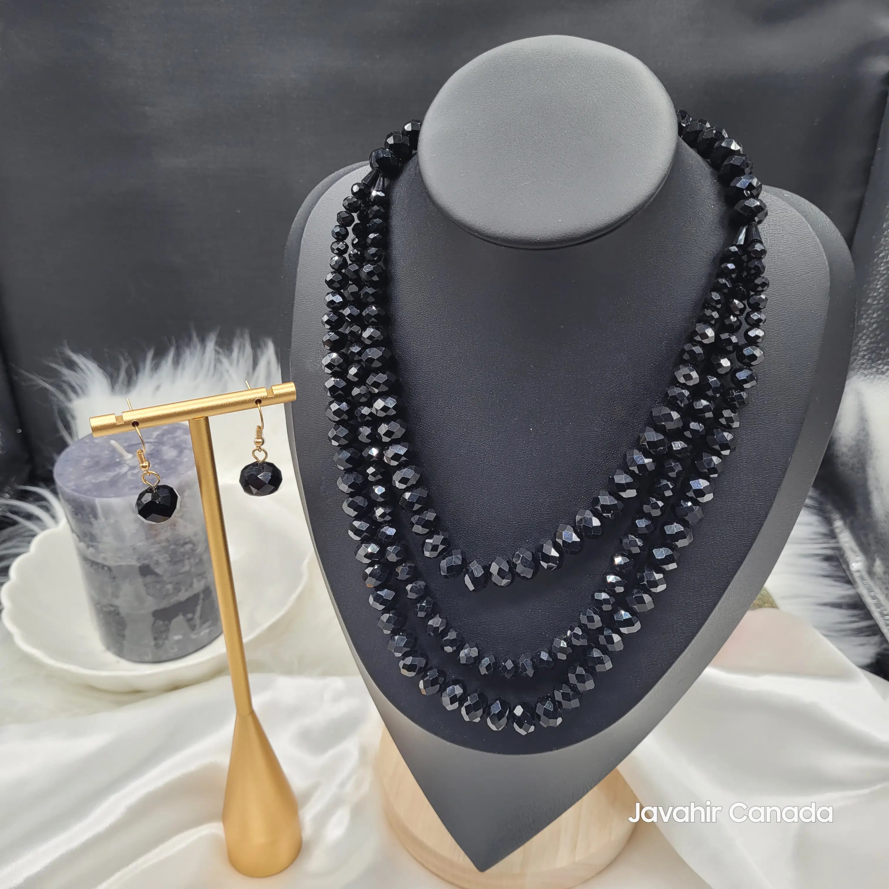 JV162 necklace set in jet black faceted glass beads with a four-strand graduated design, displayed on a black bust with matching black bead drop earrings on a gold stand.