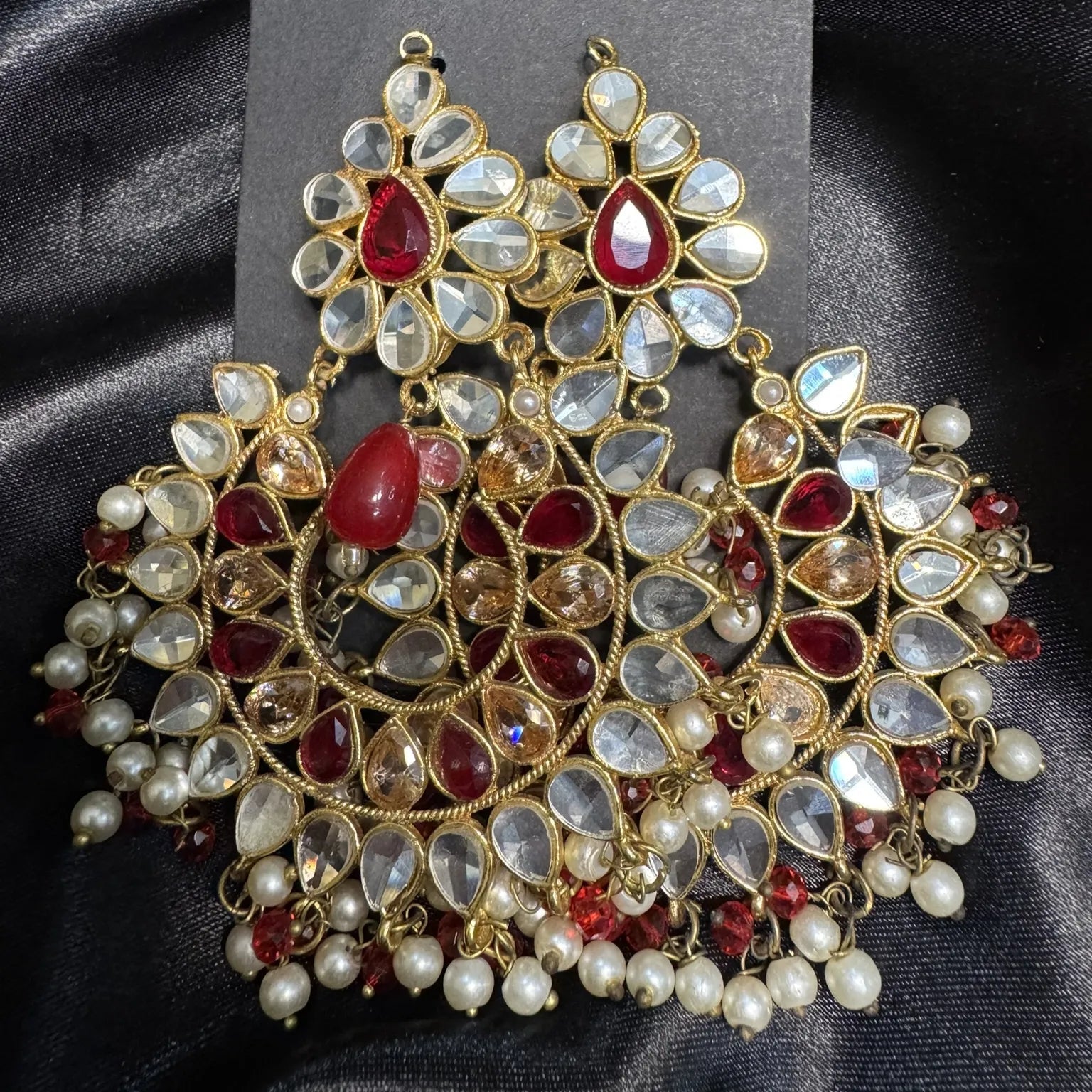 Ornate earrings with red and clear gemstones on a black card against a black satin background