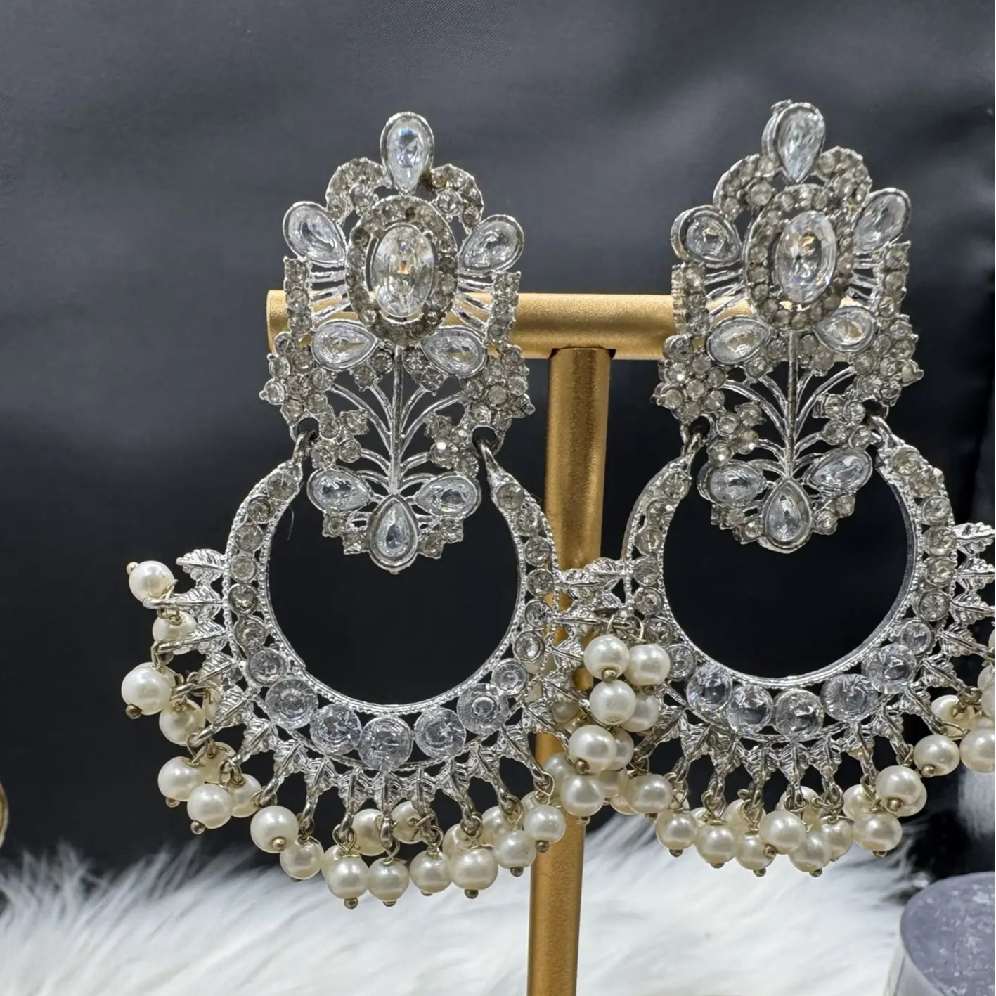 Pair of ornate Pakistani style traditional silver earrings with pearls on a stand against a dark background