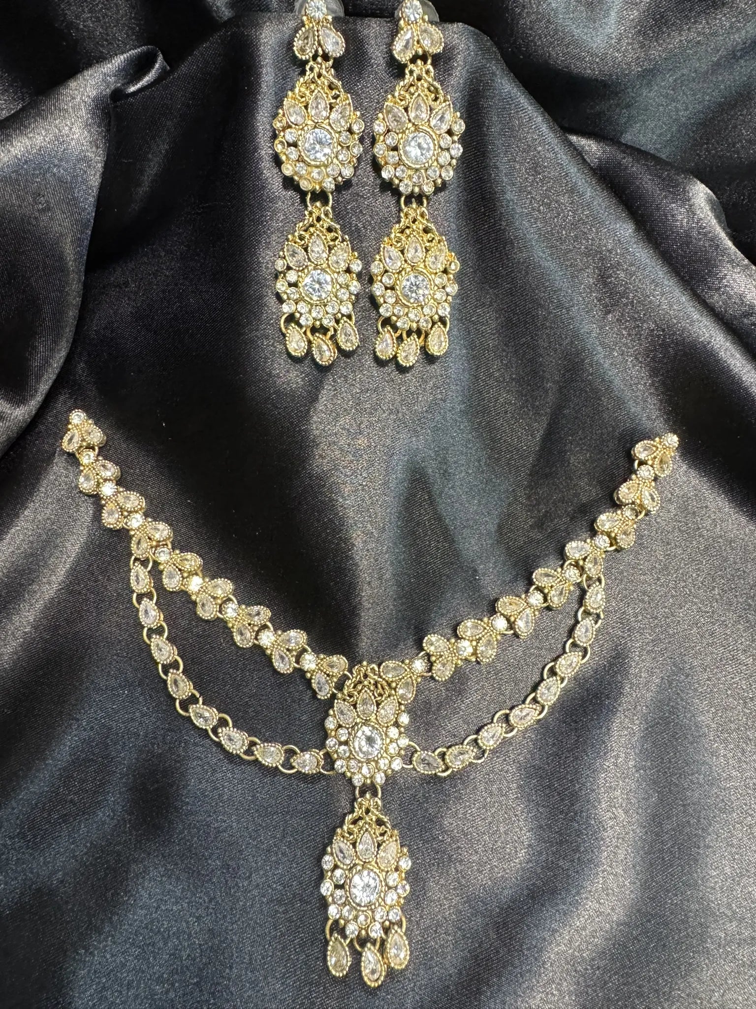 JV51 gold-plated floral necklace set with double-layered chain and matching long earrings on black satin backdrop.