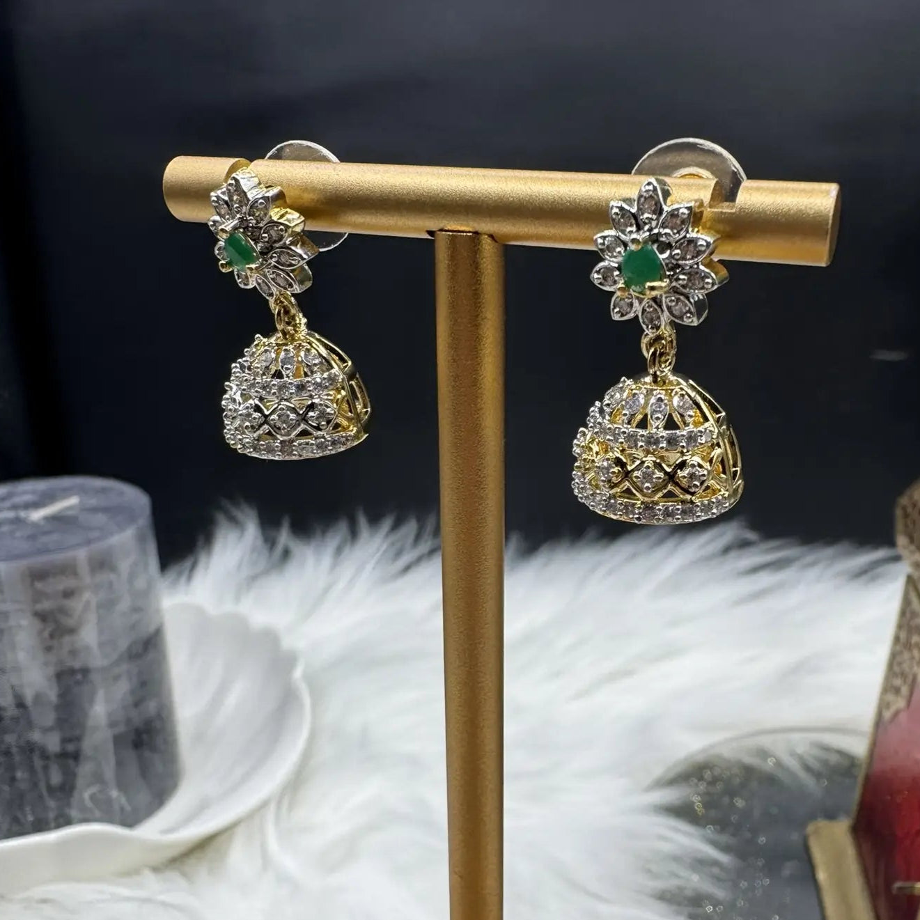 side view of Pair of Pakistani style jhumka earrings with emerald gemstones and a gold base with a blurred background