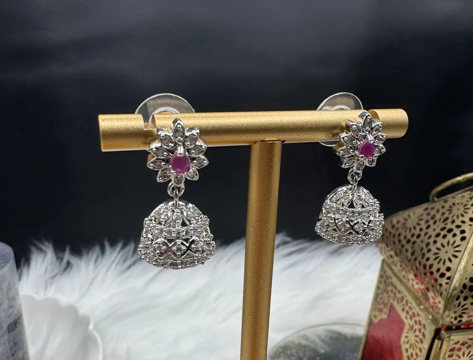 top view of Pair of Pakistani style jhumka earrings with hotpink gemstones and a silver base with a blurred background