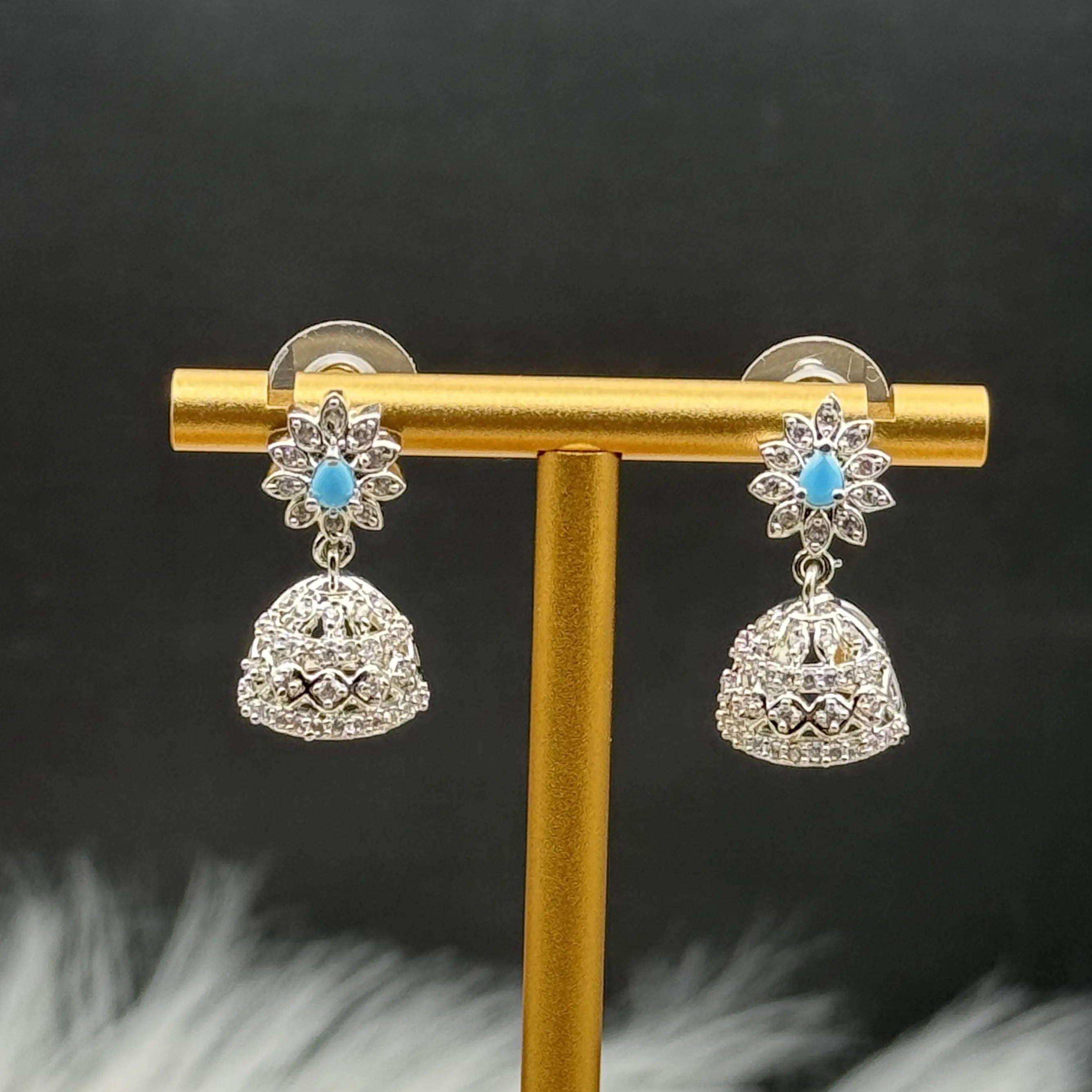 Pair of Pakistani style jhumka earrings with turquoise gemstones and a gold base on a gold earring stand against a dark background.