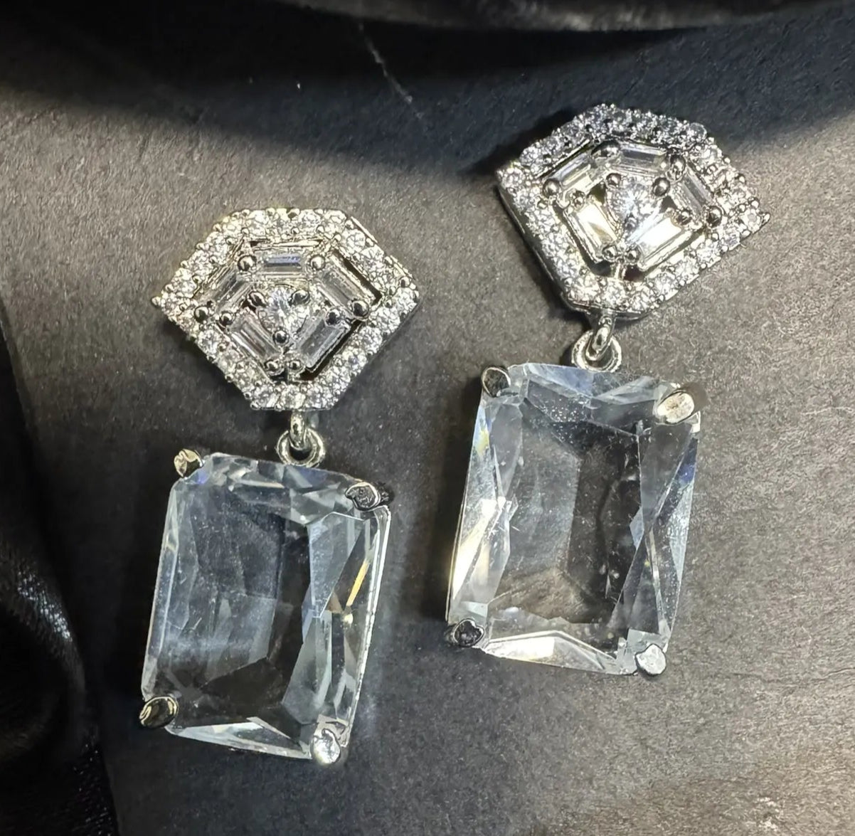 Pair of silver earrings with clear gemstones on a dark fabric background