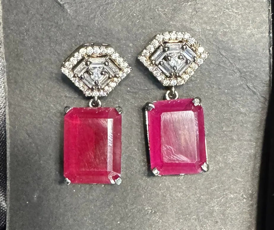 Pair of earrings with hot pink rectangular stones on a gray card against a black satin background