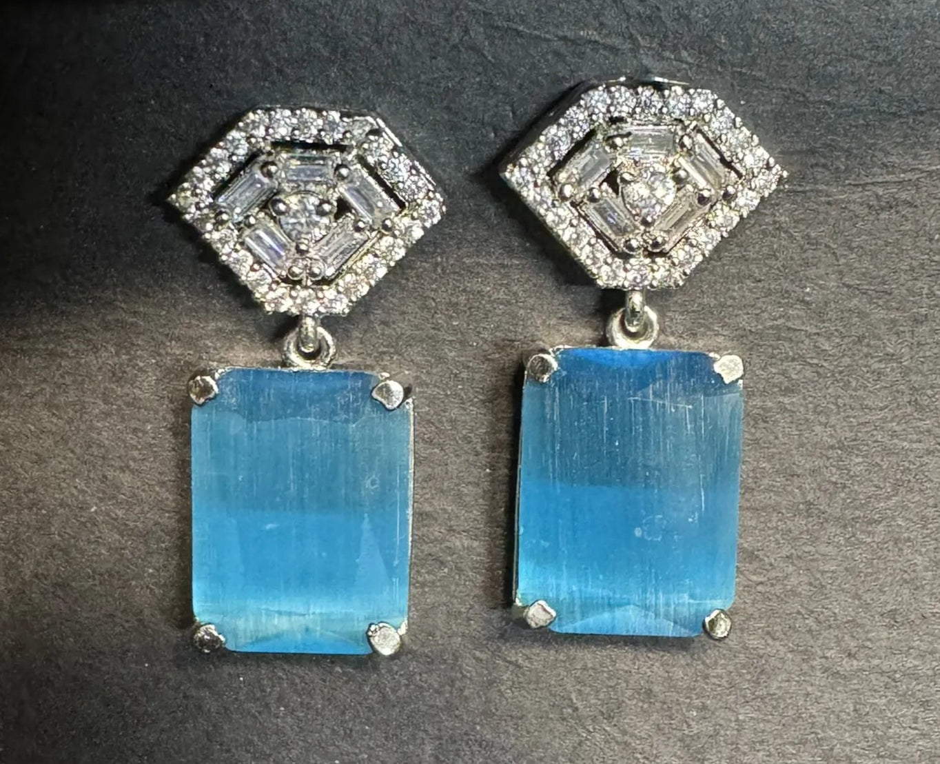 Pair of earrings with blue rectangular stones and diamond-like tops on a gray background