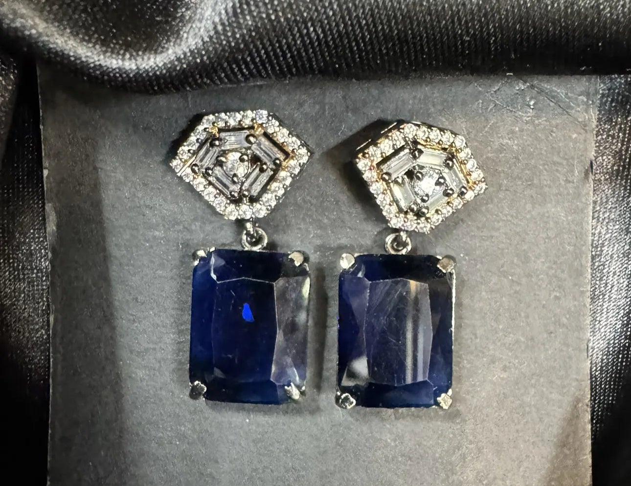 Pair of sapphire earrings with diamond-like stones on a gray background