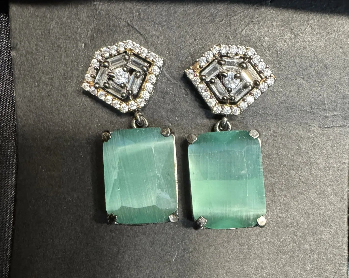 Pair of earrings with teal gemstones and diamond-like tops on a gray background