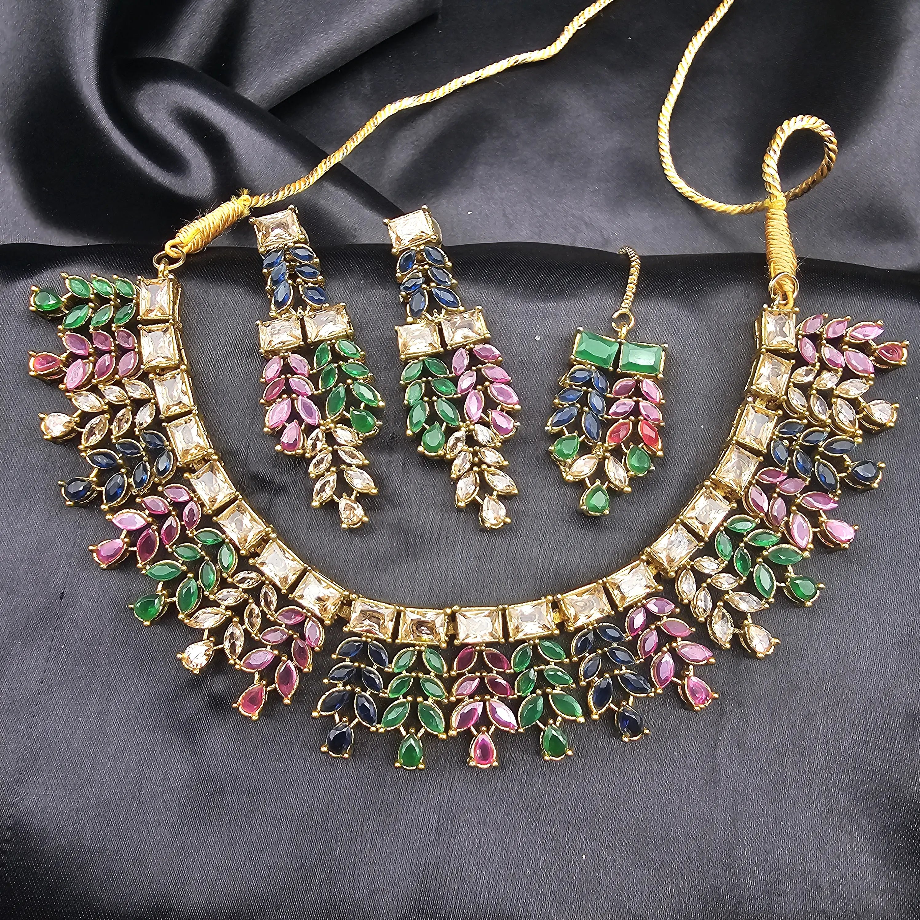 Full Kaleidoscope necklace set with multicolor leaf stones, matching earrings and tikka on black satin backdrop.