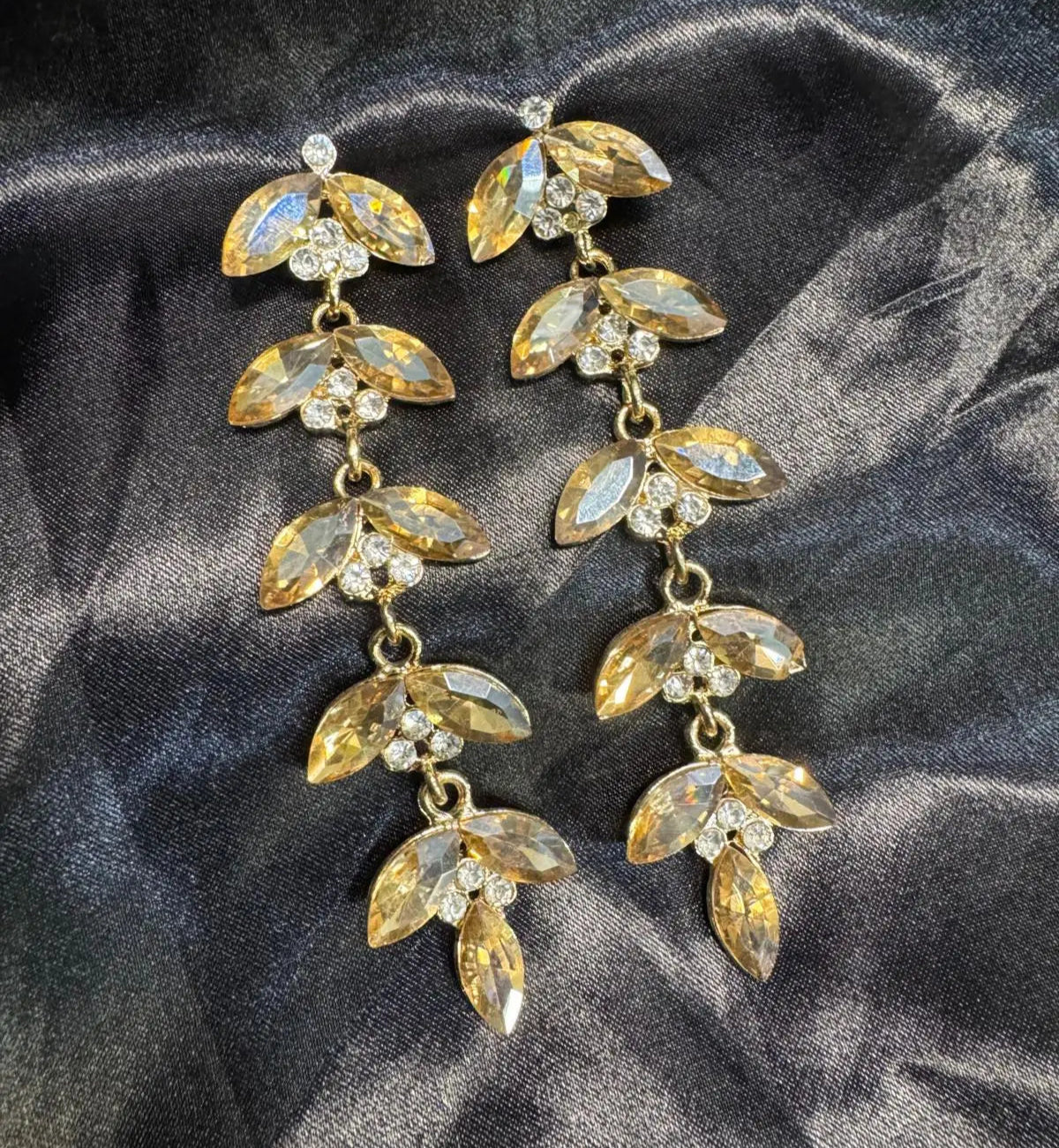 Gold plated leaf-shaped earrings with clear stones on a dark fabric background. Handcrafted in Pakistan