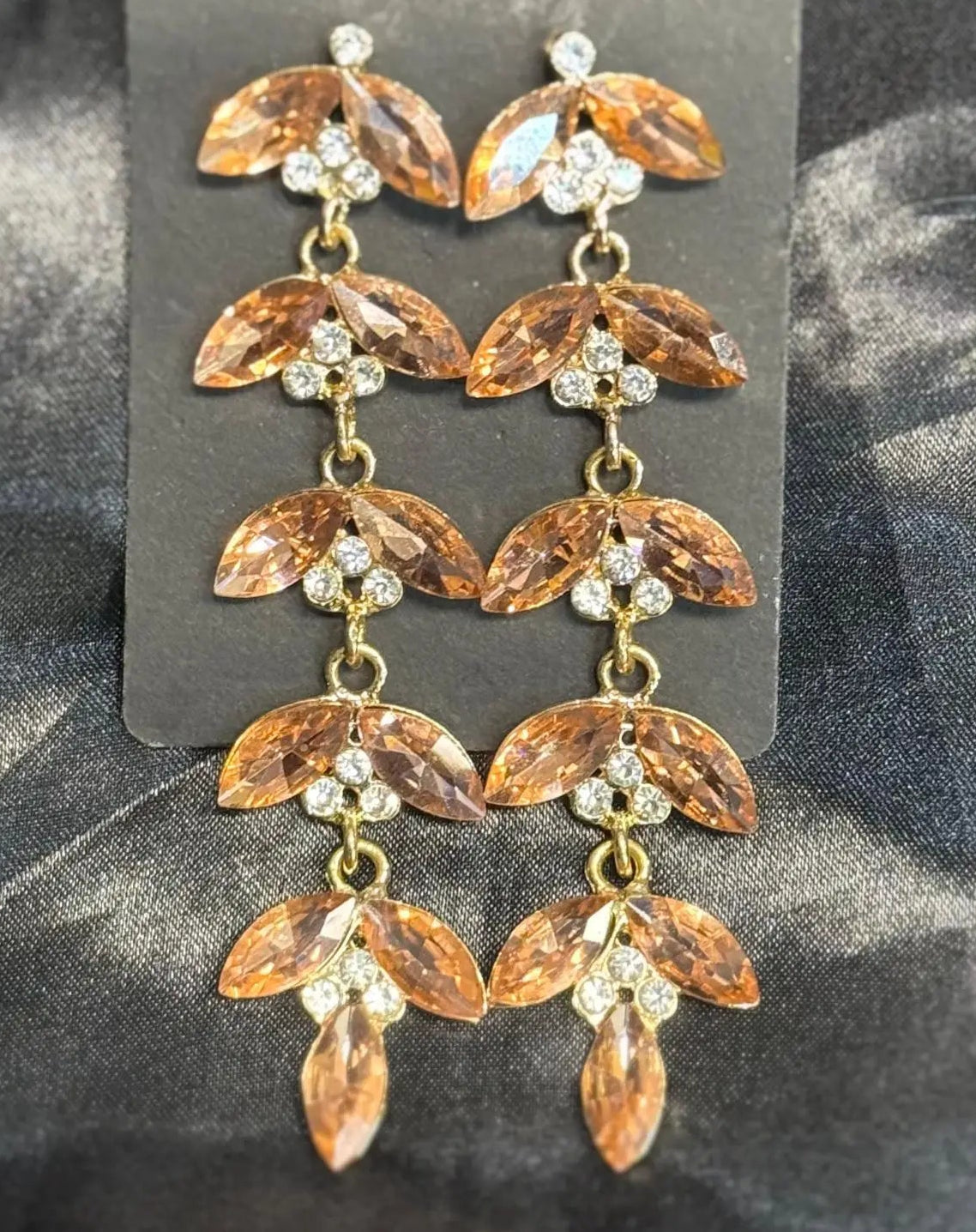 Gold plated leaf-shaped earrings with clear pink stones on a dark fabric background. Handcrafted in Pakistan