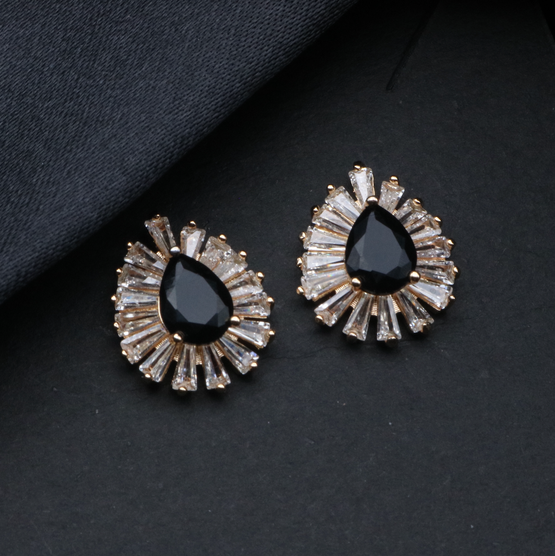 A pair of NEBULA earrings featuring a stainless steel and gold plated design with black stones and clear accent stones.