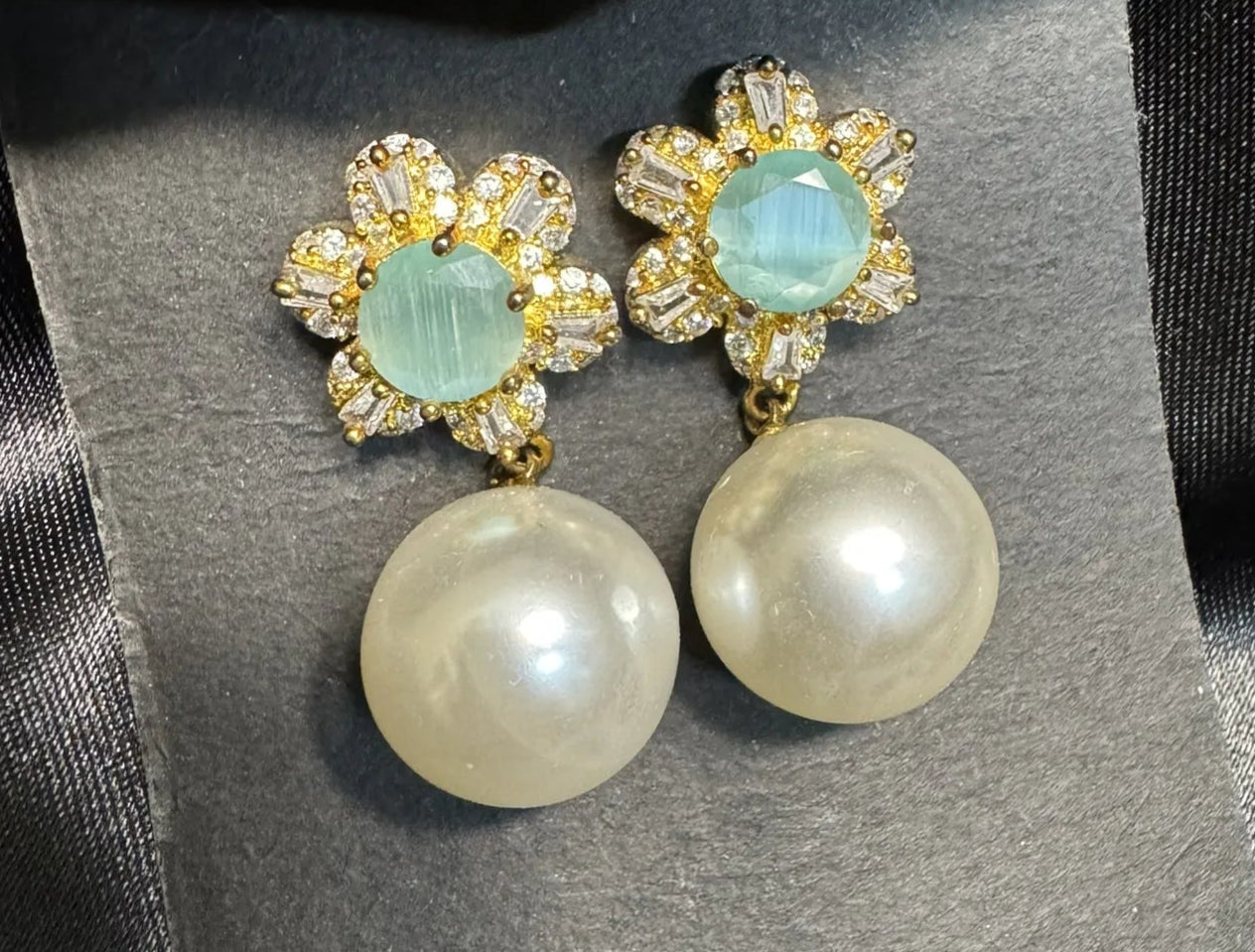 Pair of earrings with pearl-like stones and gemstone-like centers on a gray card. Handcrafted in Pakistan and are waterproof and anti-tarnish.