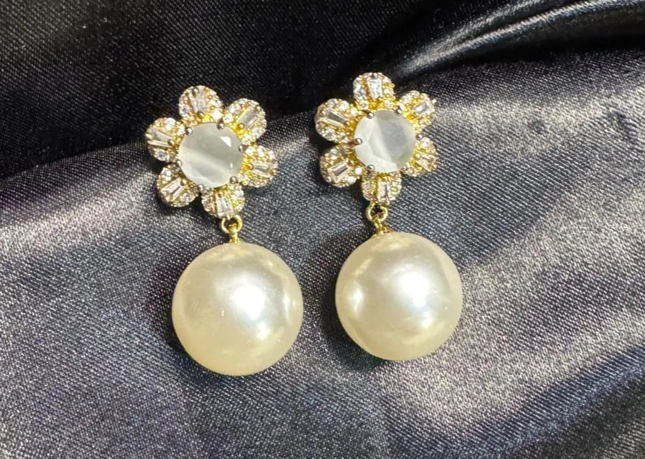 Pair of earrings with pearl-like beads and floral designs on a dark fabric background. Handcrafted in Pakistan and are waterproof and anti-tarnish.