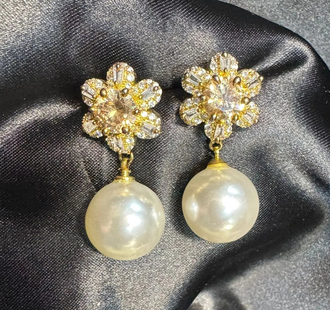 Pair of earrings with floral top and pearl bottom on a dark satin fabric background. Handcrafted in Pakistan and are waterproof and anti-tarnish.