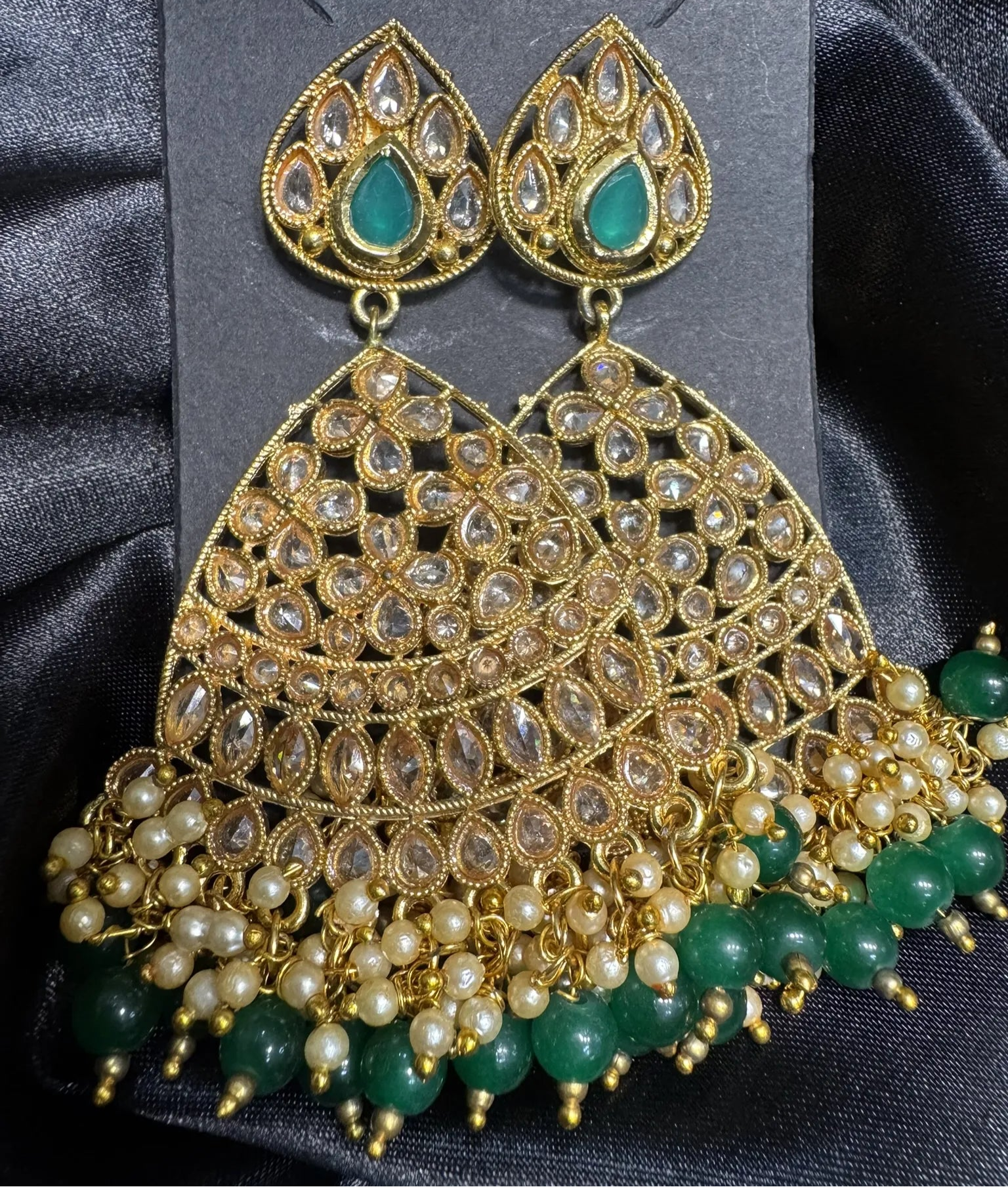 Ornate gold plated earrings with green beads on a dark fabric background