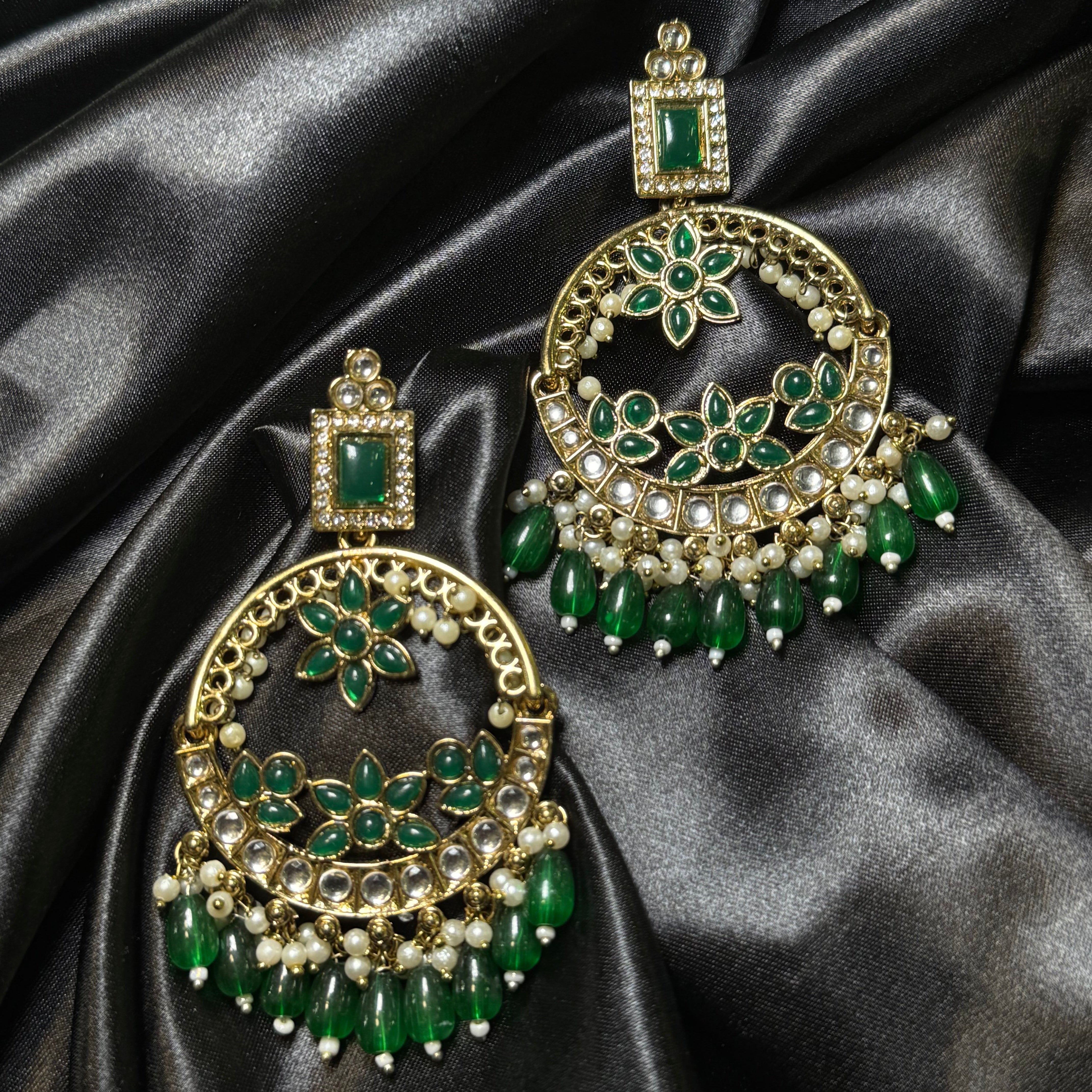 Pair of gold and green earrings on black satin fabric