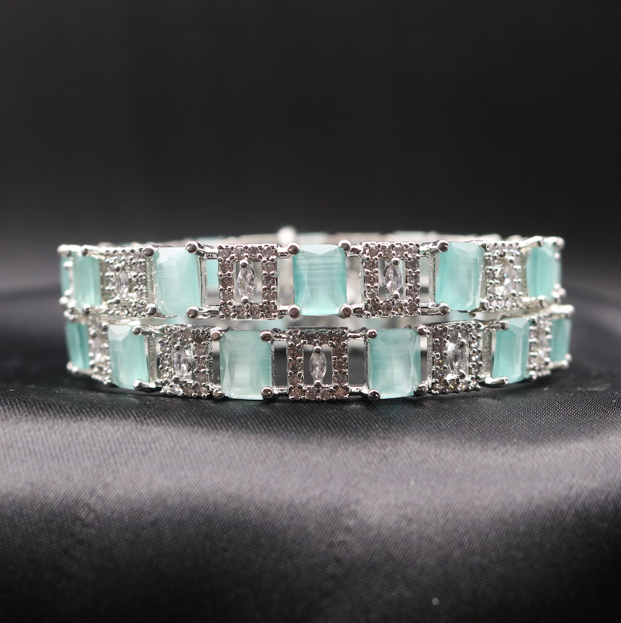 Silver bangles adorned with teal and clear stones, showcasing its sparkle and design.
