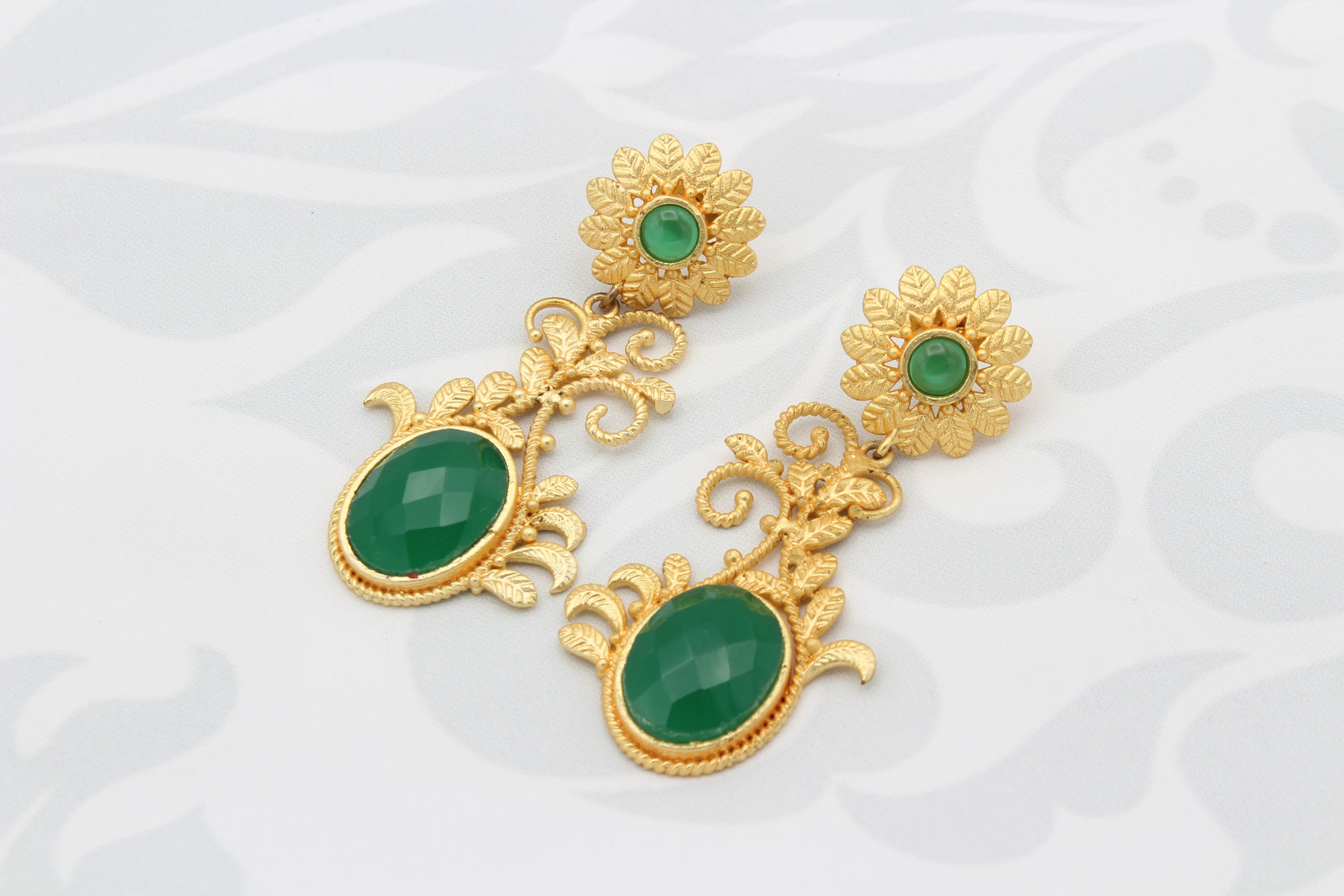Gold plated earrings with green gemstones on a white background