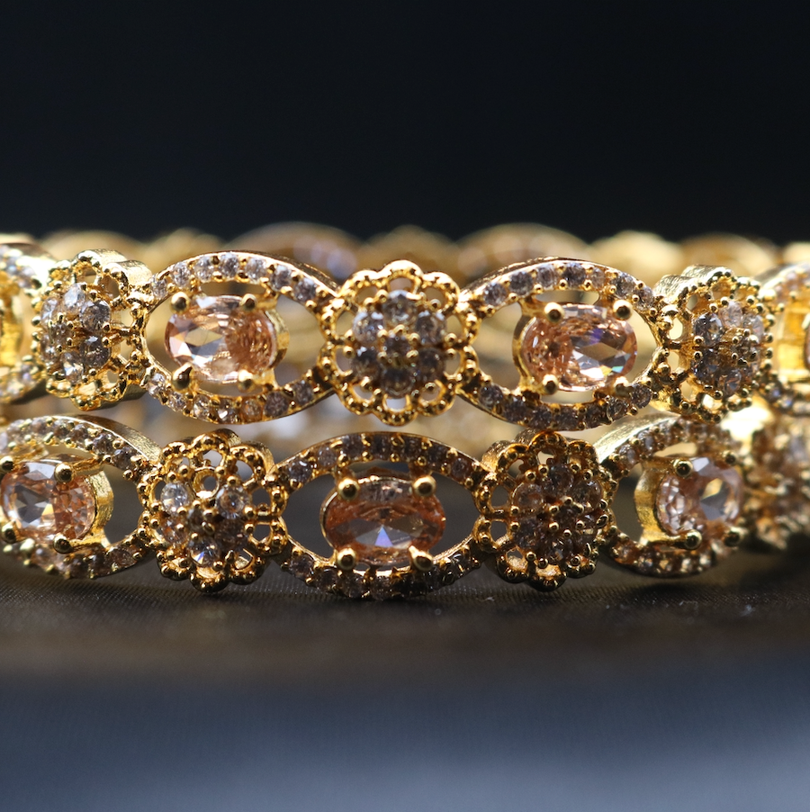 a pair of gold-plated bangles with intricate design and champagne gemstones