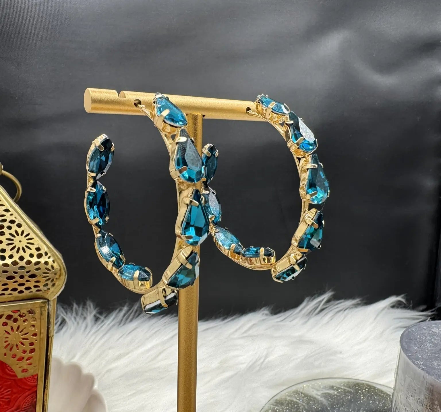 Gold hoop earrings with blue gemstones on a stand against a dark background