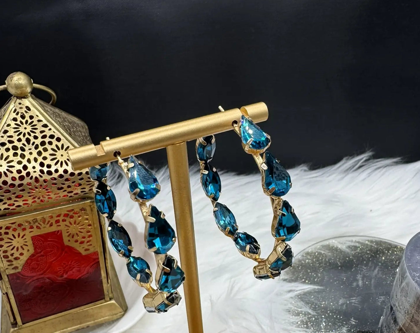 another angle of gold hoop earrings with blue gemstones on a stand against a dark background