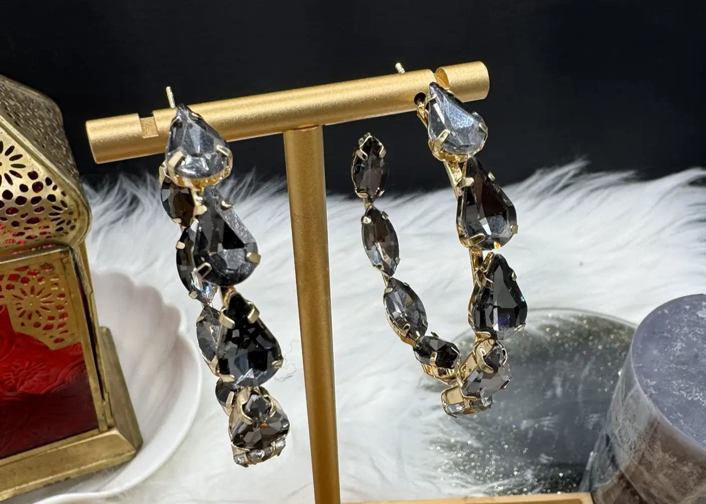 top view of Gold hoop earrings with grey gemstones on a stand against a dark background
