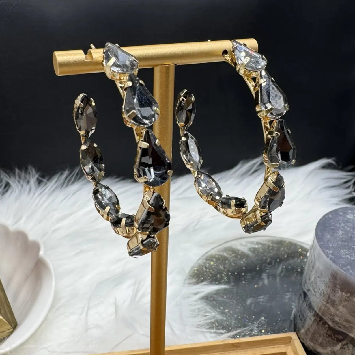 another view of Gold hoop earrings with grey gemstones on a stand against a dark background