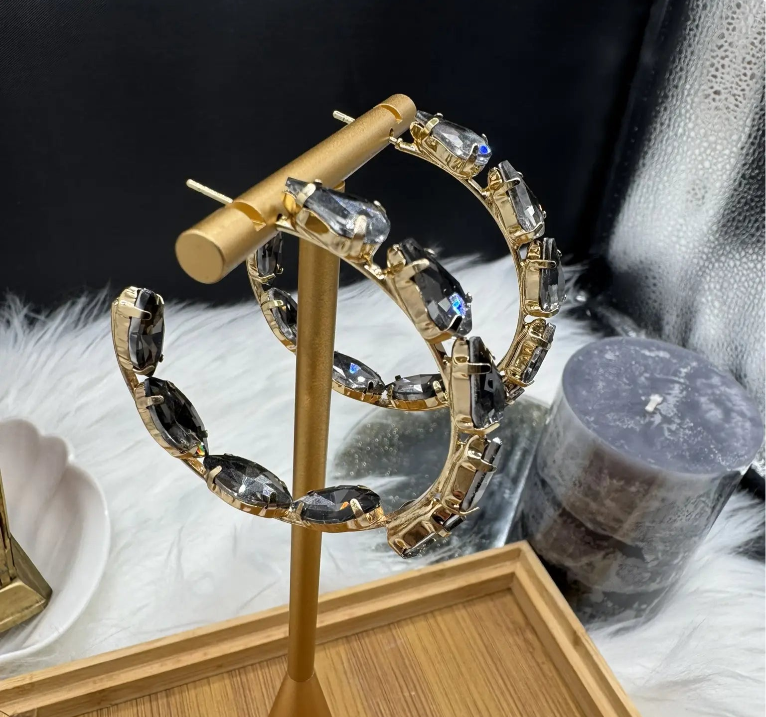 side view of gold hoop earrings with grey gemstones on a stand against a dark background