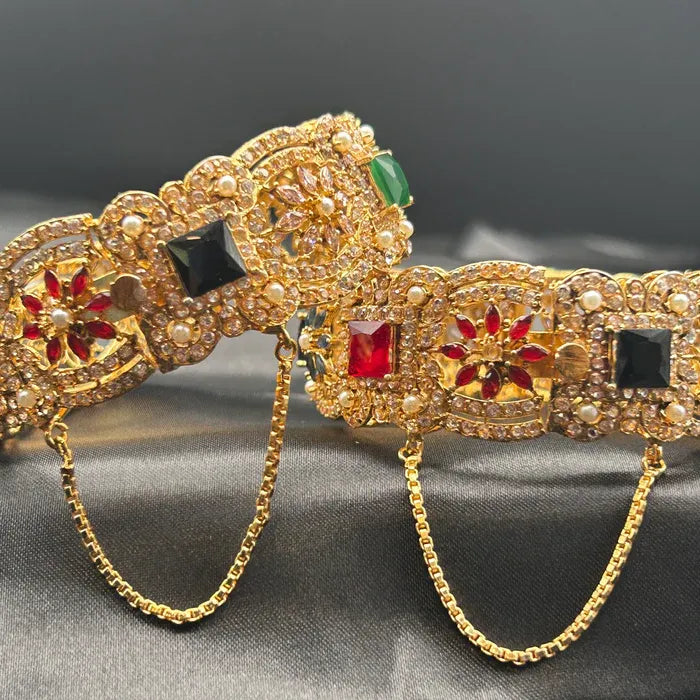 A Pakistani style Gold-plated openable bangles with red and green gemstones on a dark background