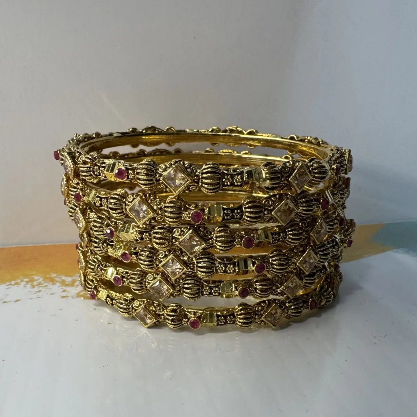Stack of gold bangles with gemstones on a white surface