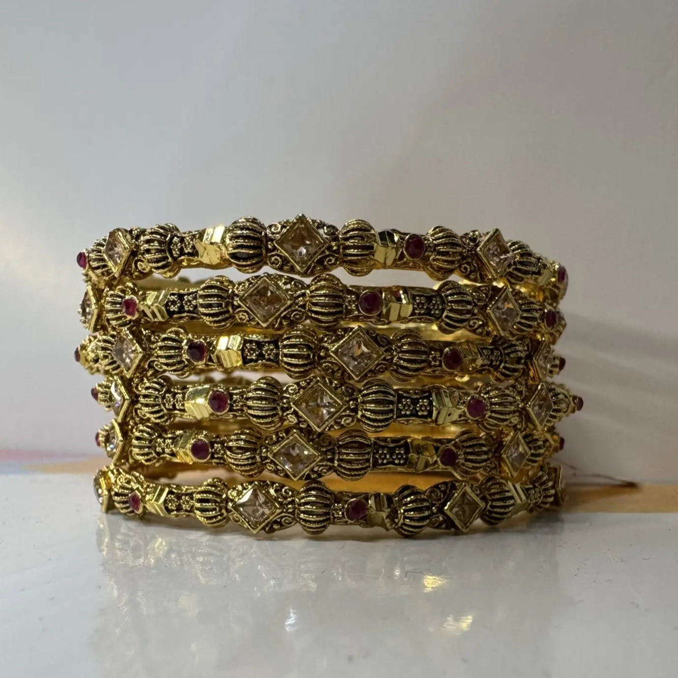 Set of gold bangles with intricate designs on a white surface