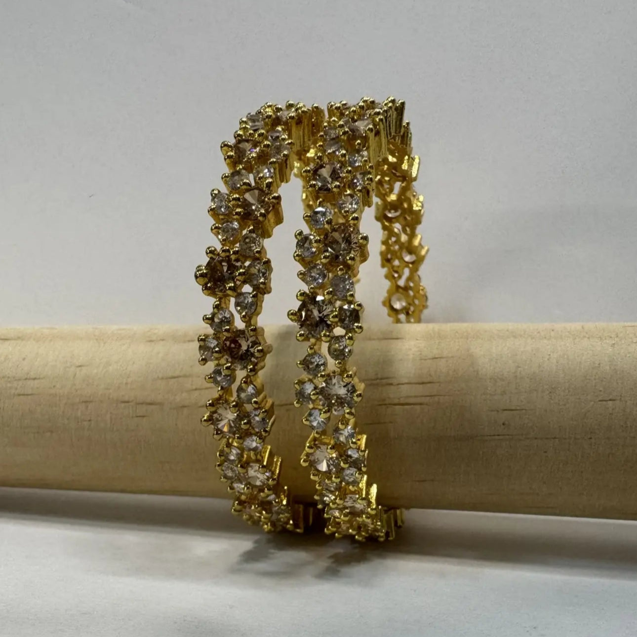 Gold-plated bangles with clear stones on a wooden stick against a gray background