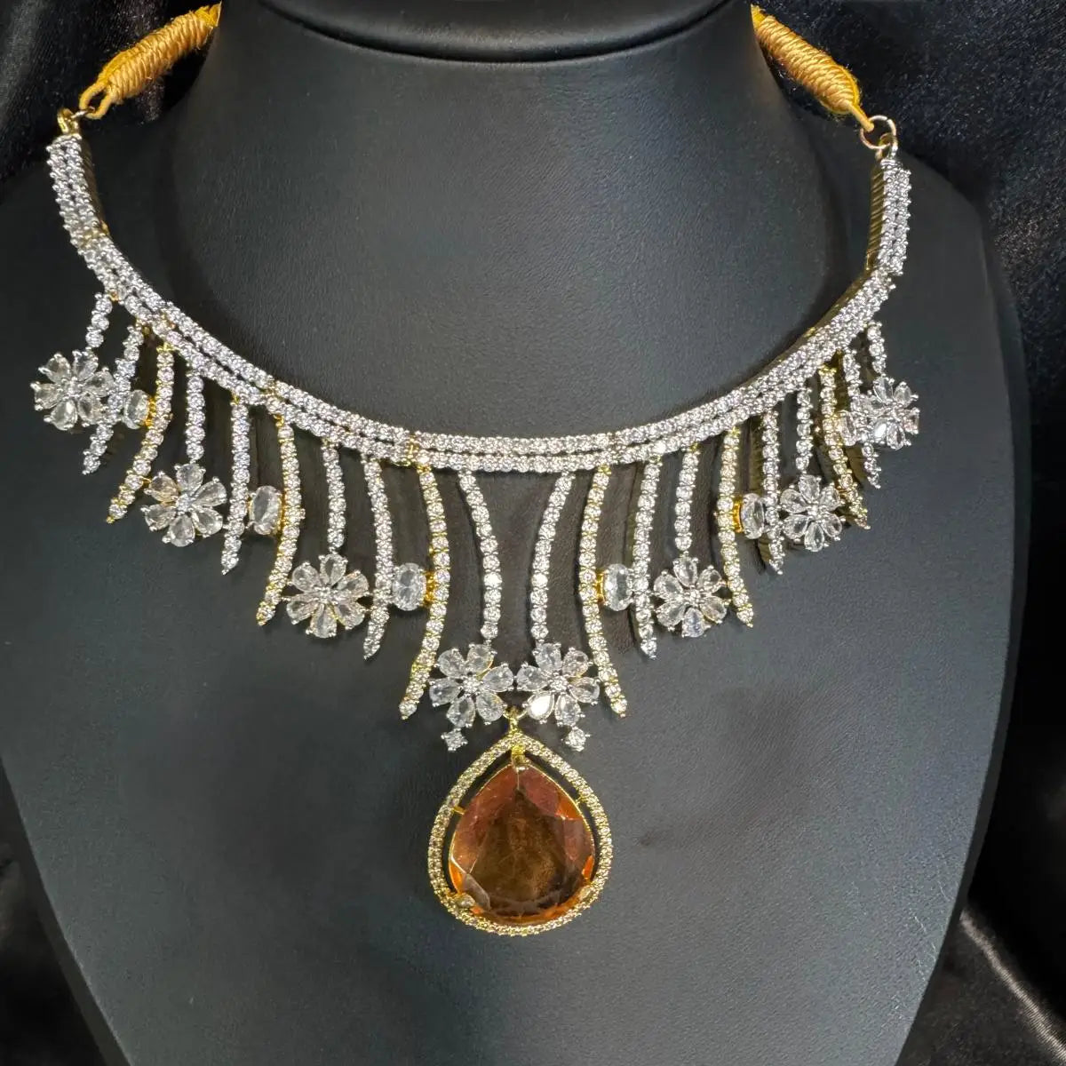 Close-up of JV159 necklace with amber teardrop pendant and floral zircon design on black display.