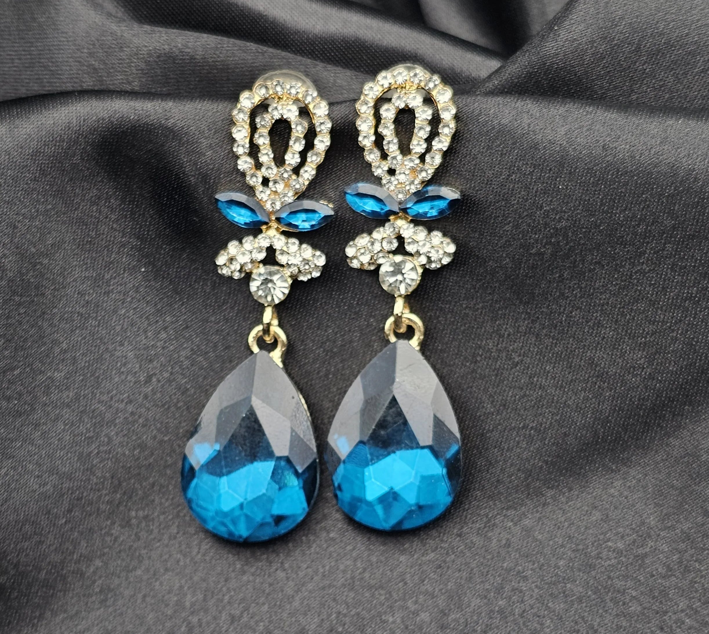 Pair of blue teardrop earrings with gold accents on a gray fabric background